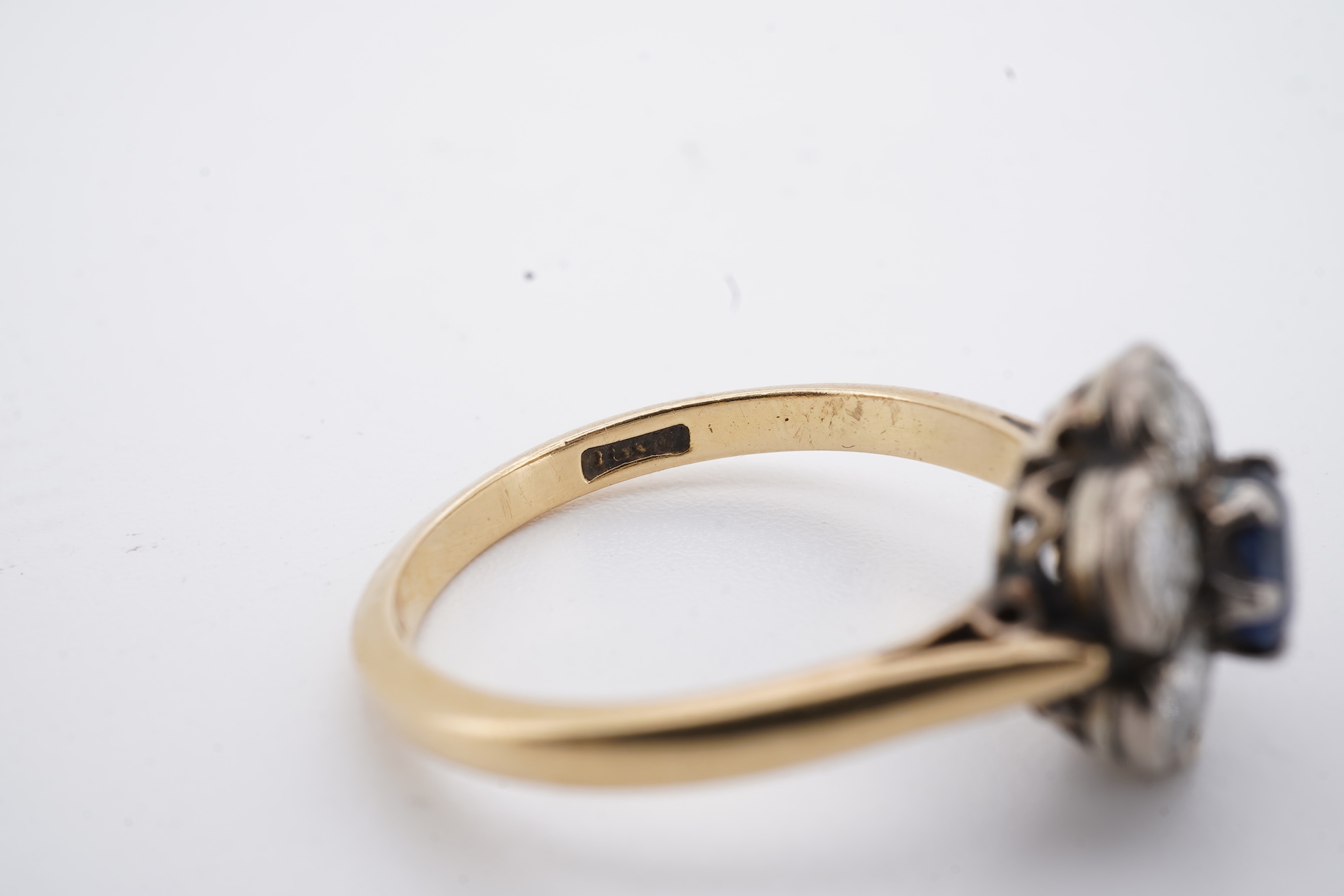 An early to mid 20th century yellow metal (stamped 18ct), singe stone sapphire and six stone diamond set circular cluster ring, size O, gross weight 3.7 grams.